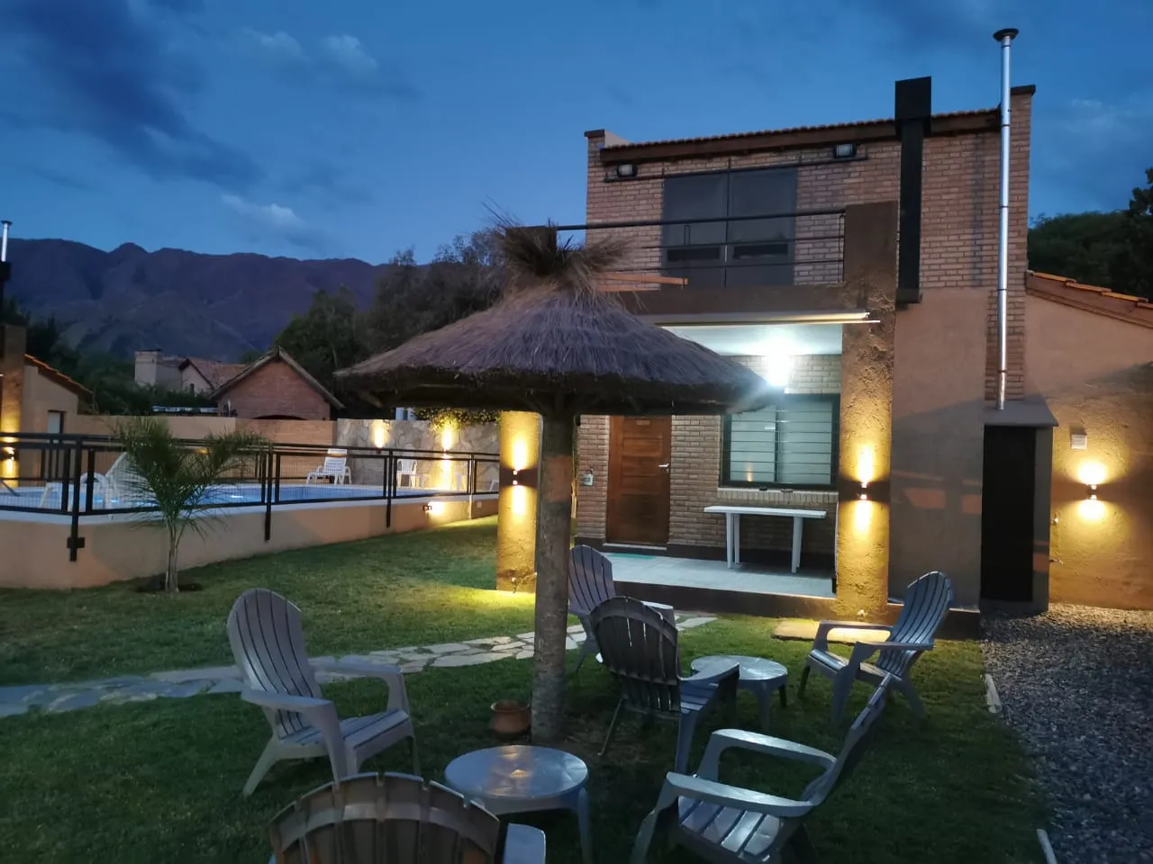 Jardín con sombrilla de paja y sillones frente a las cabañas